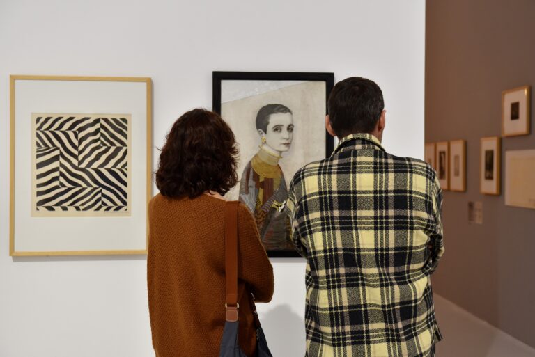 deux personnes qui regardent un tableau où l'on voit une femme qui regarde le spectateur
